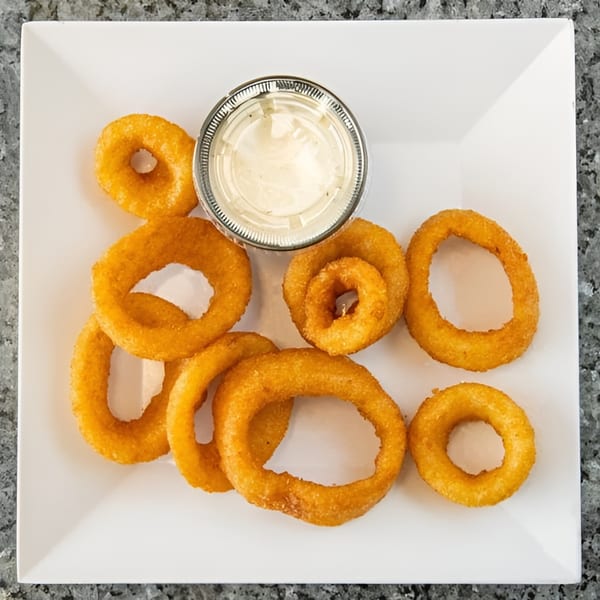 Golden-brown onion rings and a small cup of dipping sauce on a white square plate.